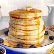 Pancake con sciroppo d'acero e mirtilli su un piatto bianco.
