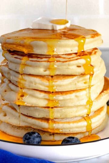 Pancake con sciroppo d'acero e mirtilli su un piatto bianco.