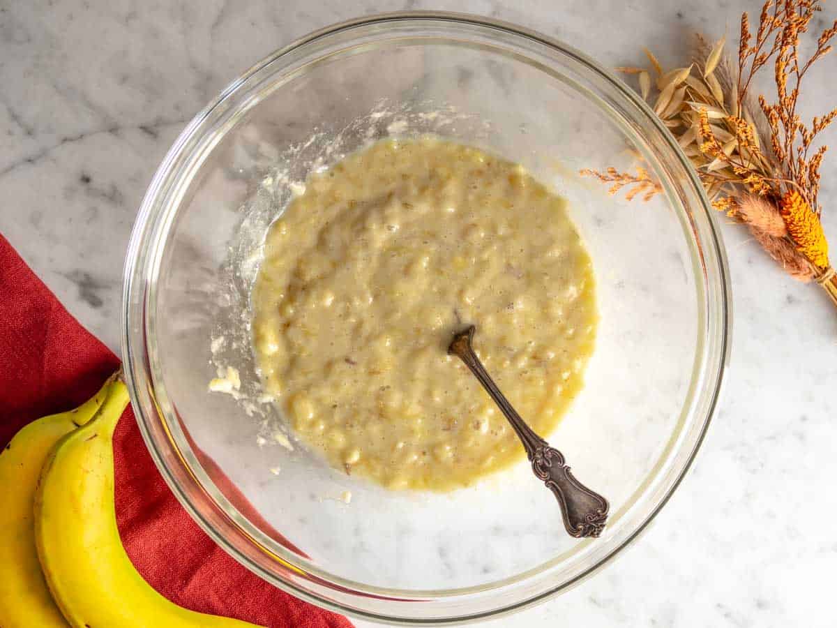Banana schiacciata insieme agli ingredienti liquidi in una ciotola.